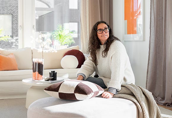 Foto på en kvinna som sitter vid en soffa i visningslägenhet på Tomtebo gård
