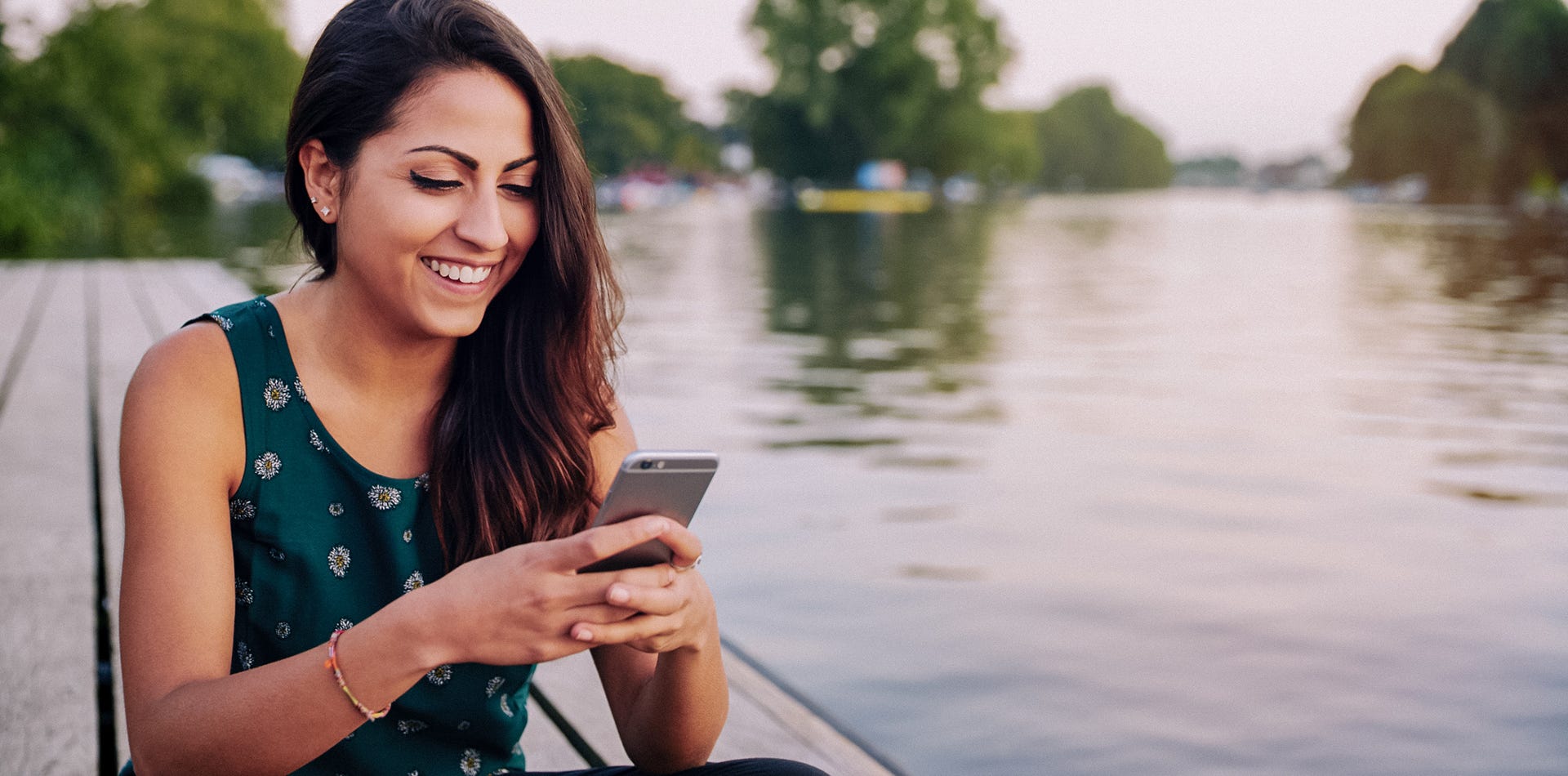 Kvinna som sitter på en brygga och läser på sin mobiltelefon