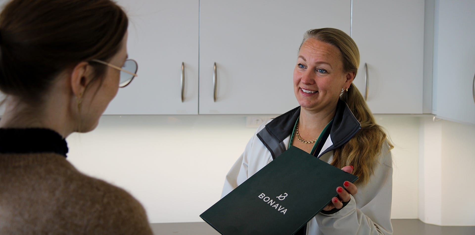 Foto på två kvinnor där den ena räcker fram en mapp till den andra