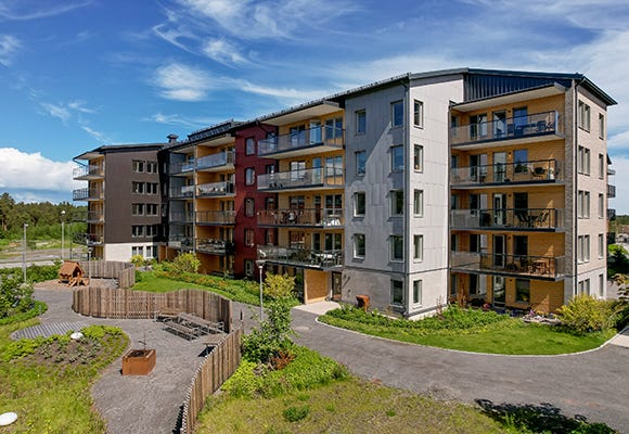 Foto på lägenhetsbyggnad med grusgångar och lekplats utanför