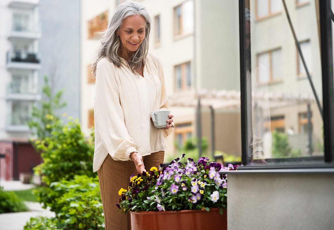 Bild på en kvinna som vattnar blommor vid ett växthus