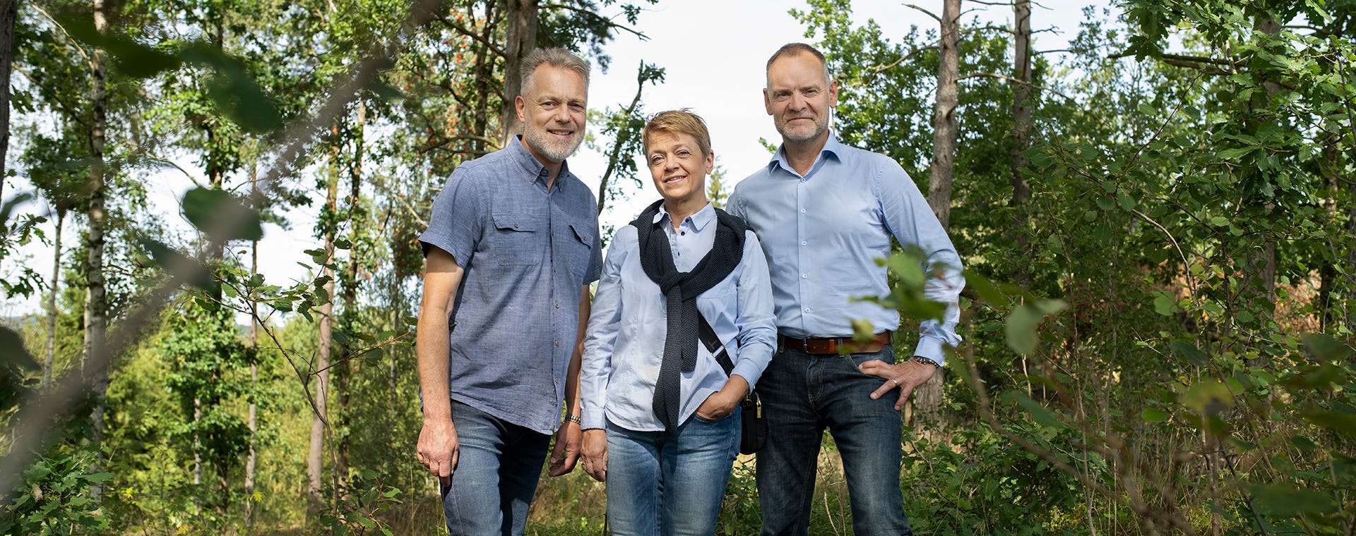Foto på tre personer som står i en skogsglänta