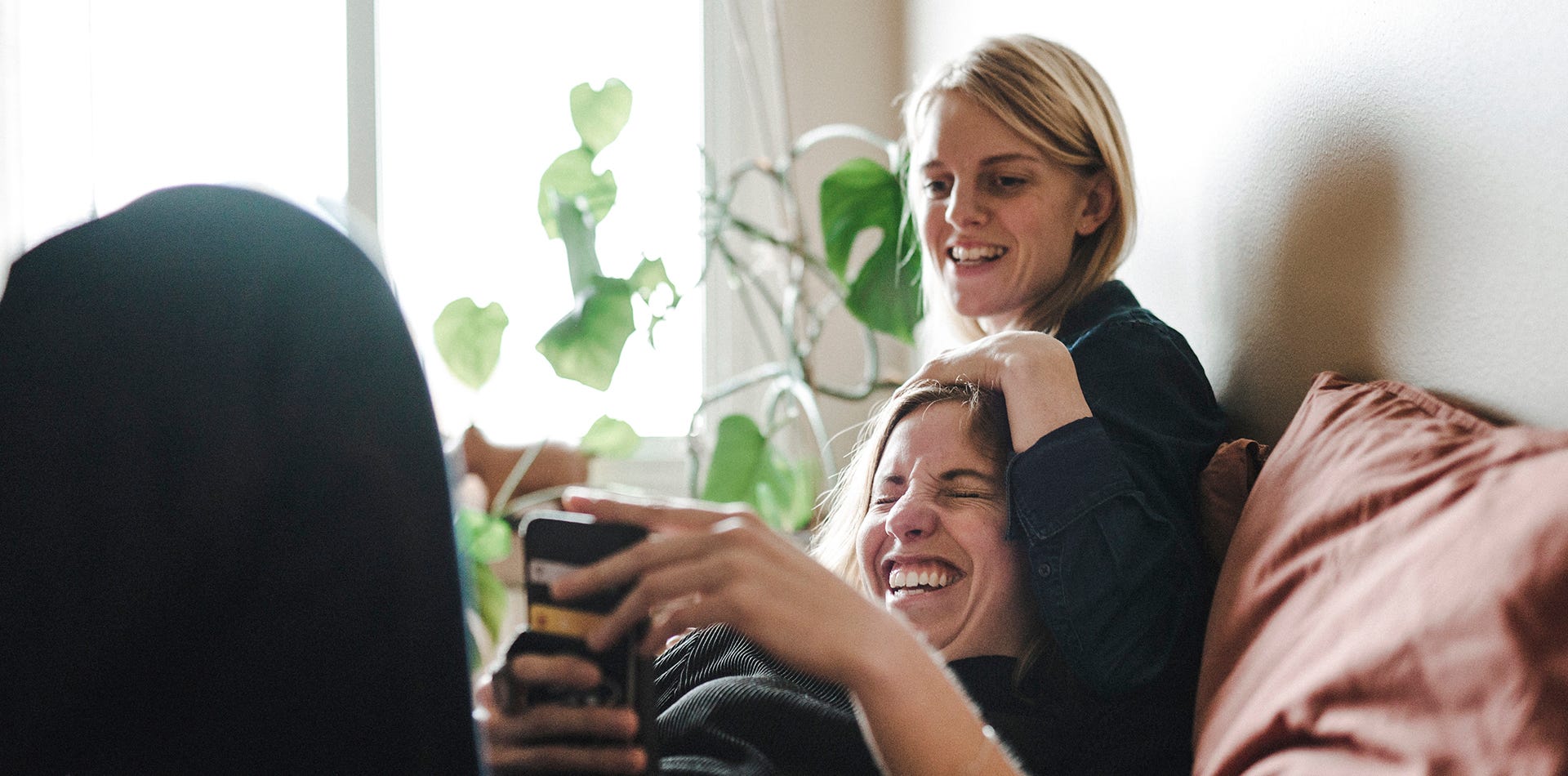 Foto på två kvinnor som sitter i en soffa och tittar på en telefon